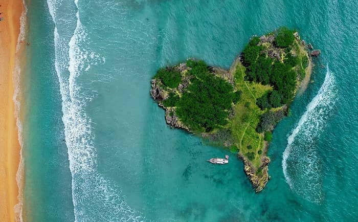 Eine kleine herzförmige und grüne Insel liegt einem Strand vorgelagert