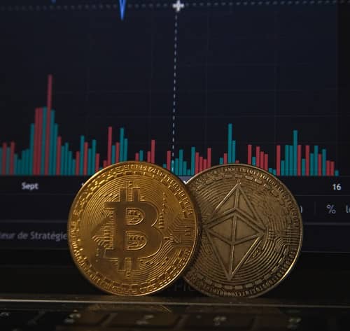 Zwei Bitcoin Münzen liegen auf einem Laptop der einen Kursverlauf anzeigt