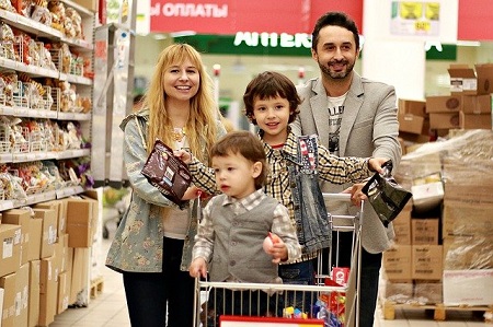 Familie mit 2 Kindern fahren mit dem Einkaufswagen vergnügt durch einen Supermarkt