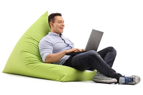 Ein Mann sitzt gemütlich in einem riesigen Sitzkissen und spielt am Laptop
