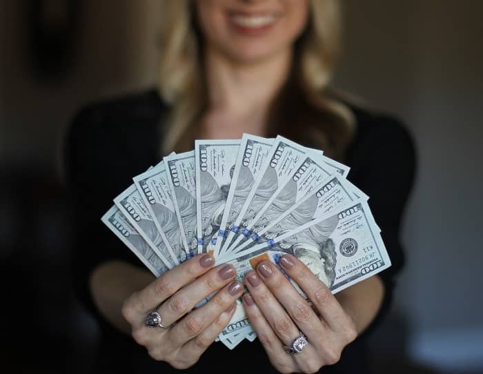 Eine Frau hält viele Geldscheine aufgefächert in die Kamerain die