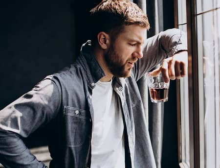 Ein Mann steht am Fenster mit einem Glas Alkohol