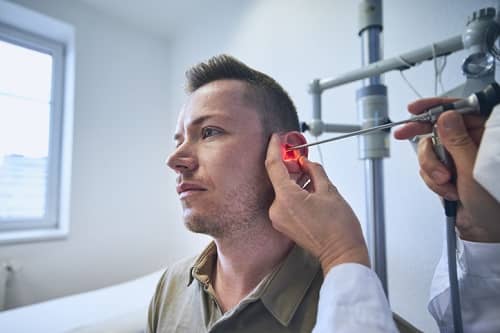Ein Mann Sitzt beim Arzt, der gerade sein Ohr untersucht