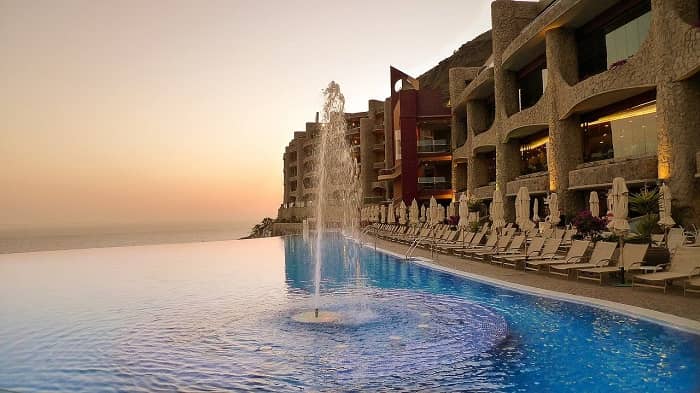 Ein Infinity Pool direkt vor einem Hotel gelegen, dahinter die untergehende Sonne