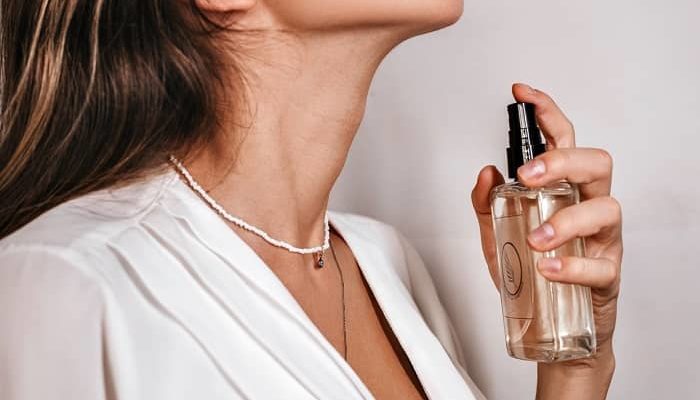 Eine Frau besprüht Ihren Hals mit einem Parfum