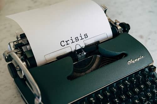 Alte Schreibmaschine mit einem Blatt Papier, auf dem Crisis geschrieben steht