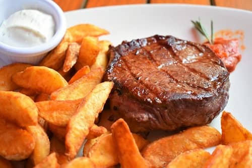 Ein Stück Fleisch mit Pommes liegt auf einem Teller