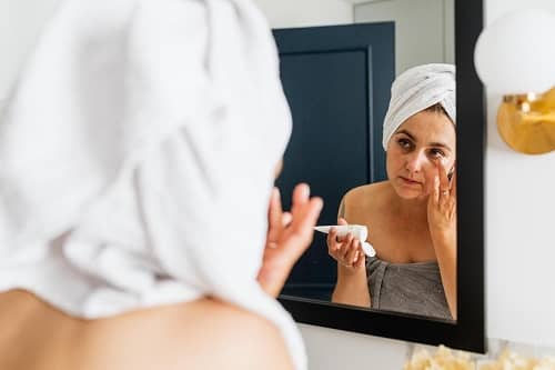 Frau steht vorm Badspiegel und cremt sich gerade unter den Augen ein