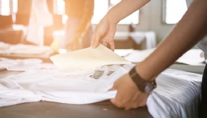 Hände bearbeiten gerade ein Shirt, das gerade bedruckt wurde