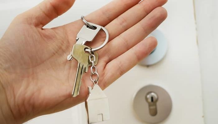 Eine Frau hält vor einer Haustüre einen Schlüssel in der Hand