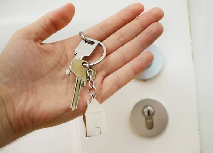 Eine Frau hält vor einer Haustüre einen Schlüssel in der Hand