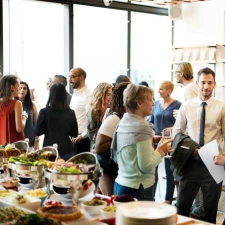 Mehrere Personen stehen bei einer Firmenfeier, neben einem Buffet, zusammen