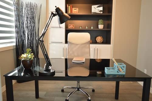 Ein großer schwarz glänzender Schreibtisch, dahinter ein weißer Bürodrehstuhl