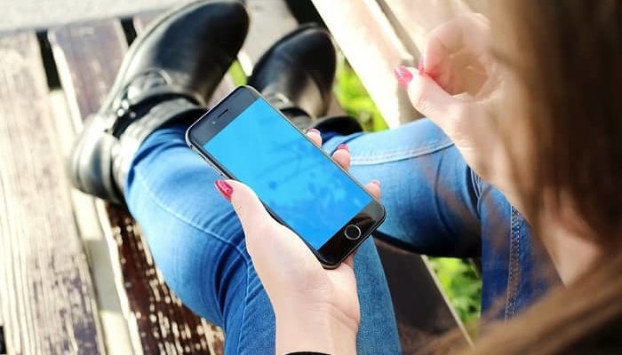 Frau sitzt auf einer Parkbank und betätigt Ihr Handy