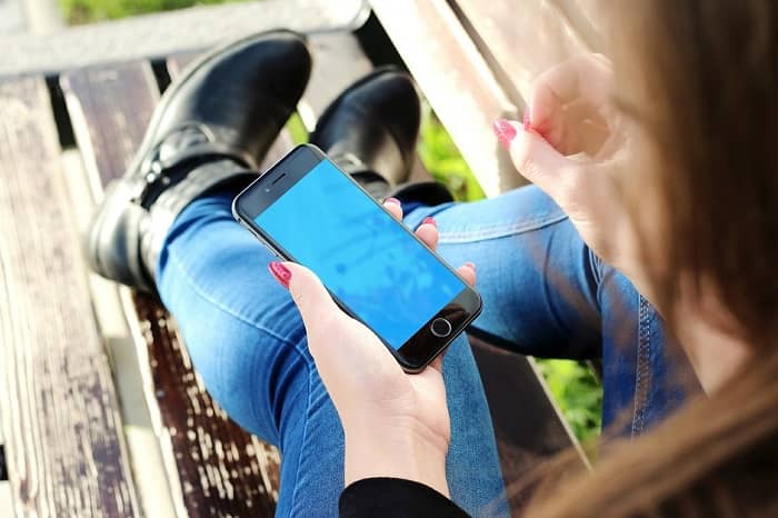 Frau sitzt auf einer Parkbank und betätigt Ihr Handy