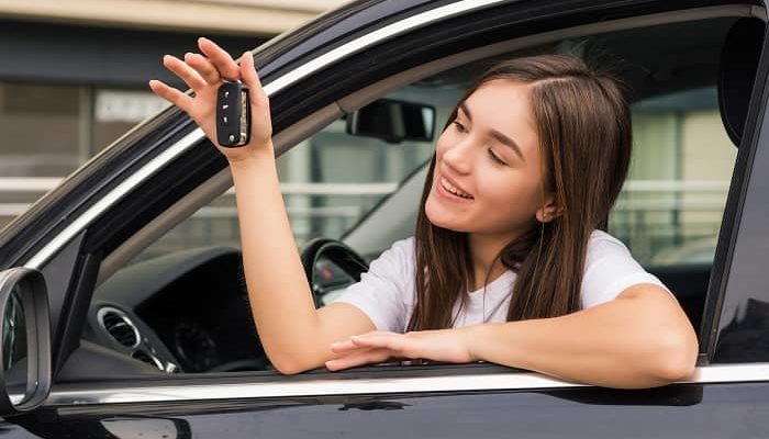 Junge Frau sitzt in einem Auto und hält einen Schlüßel in der Hand