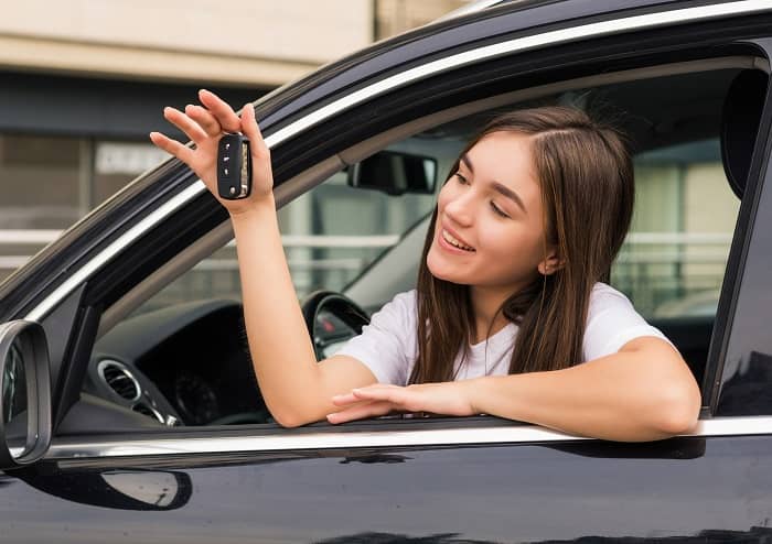 Junge Frau sitzt in einem Auto und hält einen Schlüßel in der Hand