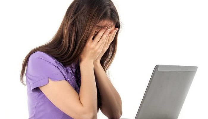 Frau sitzt resigniert, mit Ihren Händen vor dem Gesicht, vor Ihrem Laptop