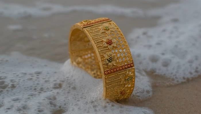 Ein goldener Ring steht im Sand und wird von Meerwasser umspült