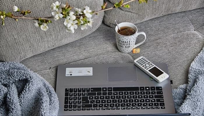 Ein Laptop, ein Telefon und eine Tasse Tee stehen auf einem Sofa