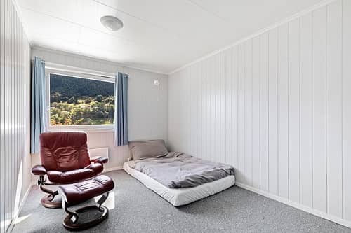 Ein Zimmer mit einem Bett und einem Sessel, in dem eine Wand komplett mit hellgrauen Paneelen verkleidet ist