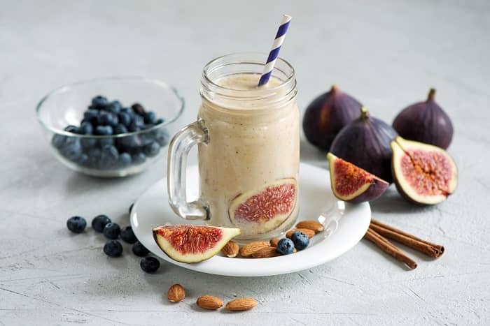 Ein Shake mit einer Feige darin, steht umgeben von Blaubeeren, Mandeln und Feigen auf einem Tisch