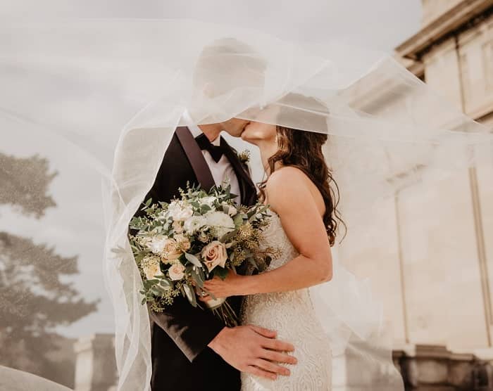 Ein Brautpaar steht vor einem alten Bauwerk und küsst sich