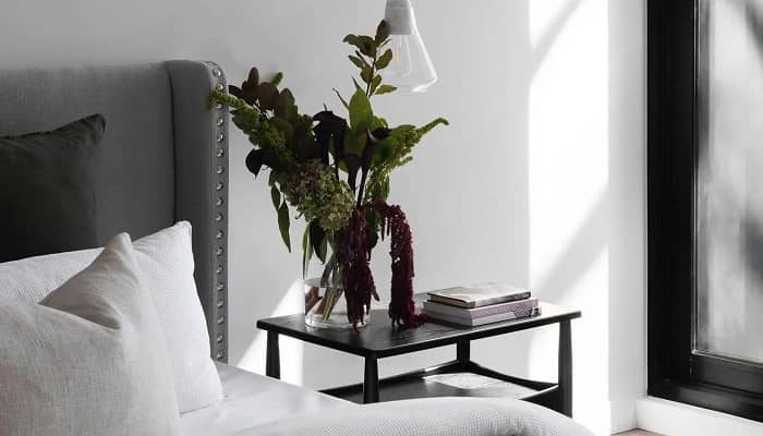 Ein schönes Bett mit einem Nachttischchen, auf dem eine schöne Vase steht