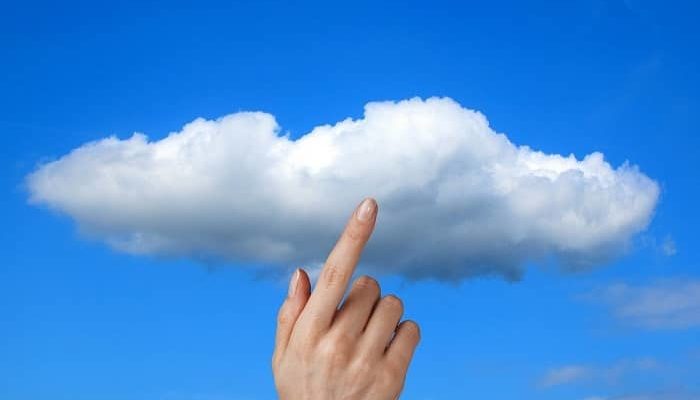 Eine Hand die auf eine Wolke vor blauem Himmel zeigt