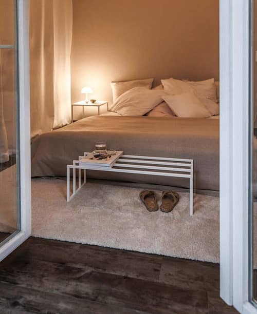 Blick von einer Terasse in ein Schlafzimmer, dort steht ein großes Bett mit vielen Kissen