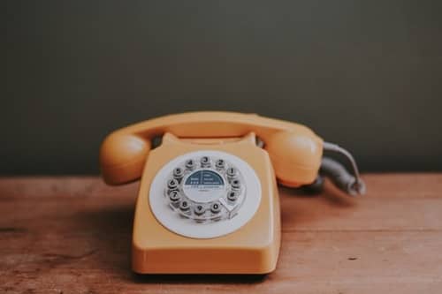 Ein altes oranges Telefon mit Wählscheibe steht auf einem Tisch