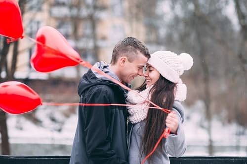 Ein junges Paar, Gesicht an Gesicht mit roten Luftballons in der Hand