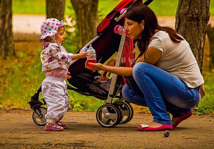 Eine Mutter überreicht, vor einem Buggy, Ihrer Tochter die Nuckelflasche