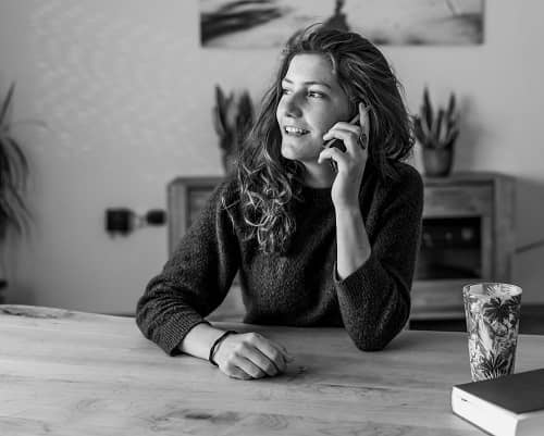 Eine junge Frau sitzt am Esstisch und telefoniert mit einem Handy