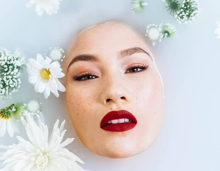 Das Gesicht einer Frau, das in einem Pflegebad mit verschiedenen Blüten und Pflanzen schwimmt