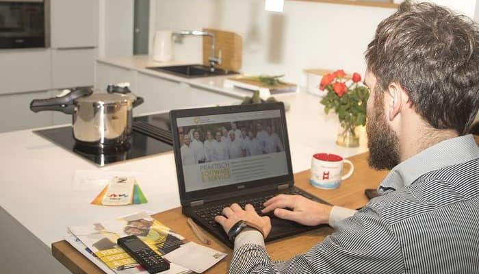 Ein Mann sitzt mit seinem Laptop in der Küche und arbeitet