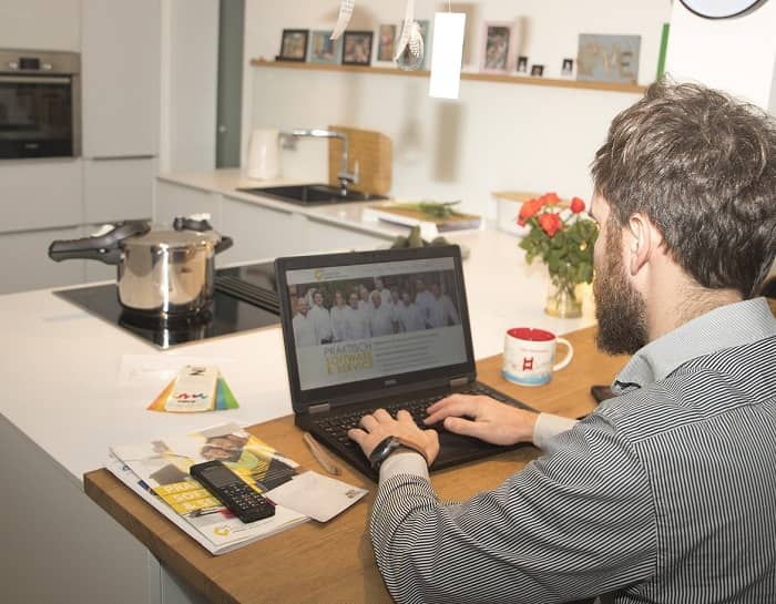 Ein Mann sitzt mit seinem Laptop in der Küche und arbeitet