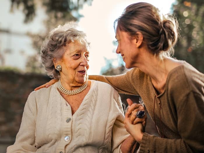 Eine junge Frau kümmert sich um eine Seniorin und drückt deren Hand