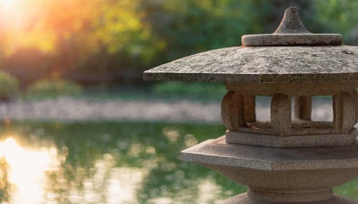 Eine Skulptur im Motiv eines Tempels steht vor einem Teich im Garten