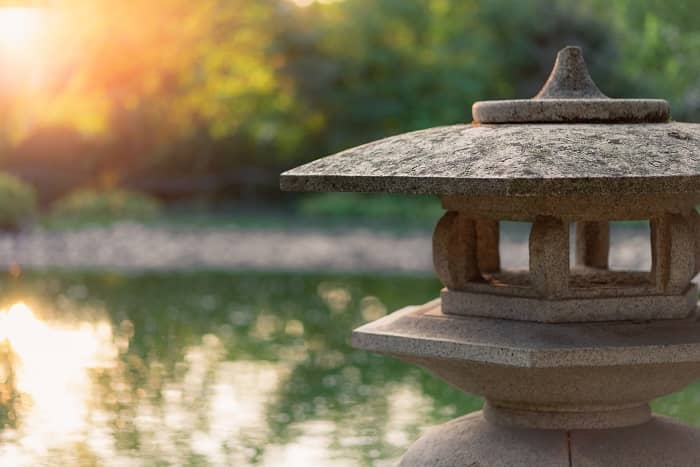 Eine Skulptur im Motiv eines Tempels steht vor einem Teich im Garten