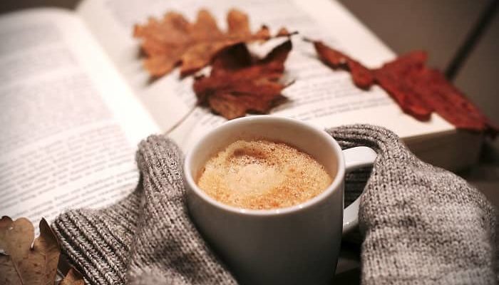 Eine Tasse Kaffee steht vor einem Buch auf dem Herbstblätter liegen