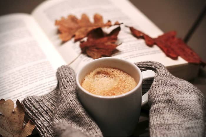 Eine Tasse Kaffee steht vor einem Buch auf dem Herbstblätter liegen