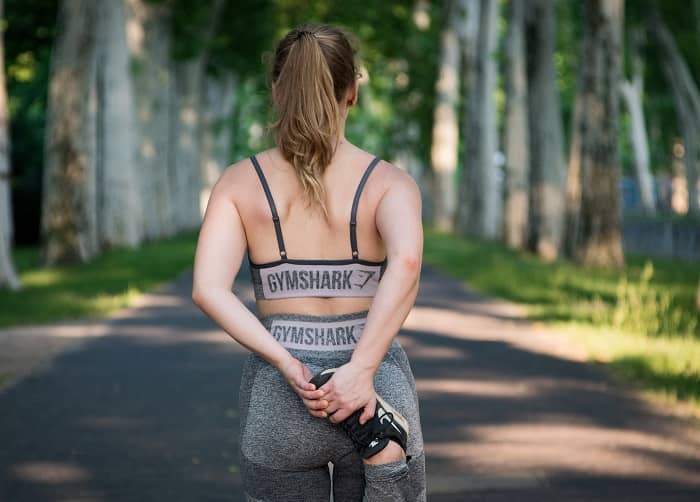 Eine Frau beim Sport in Rückenansicht, dehnt gerade Ihr rechtes Bein