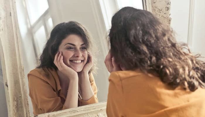 Eine Frau schaut in einen Süpiegel und lächelt selbstzufrieden