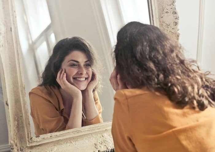Eine Frau schaut in einen Süpiegel und lächelt selbstzufrieden
