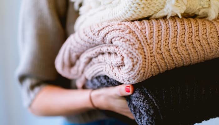 Eine Frau trägt drei dicke Strickpullover zum Schrank