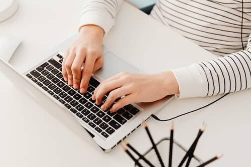 Eine Frau sitzt am Tisch und schreibt einen Lebenslauf auf Ihrem Laptop