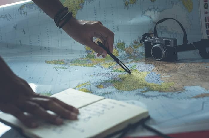 Eine Person zeigt mit einem Stift auf eine Landkarte, daneben liegt ein Fotoapparat und ein Notizbuch