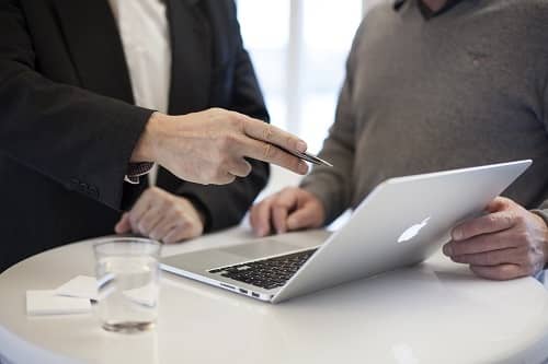 Zwei Männer stehen mit einem Laptop an einem Tisch und besprechen etwas