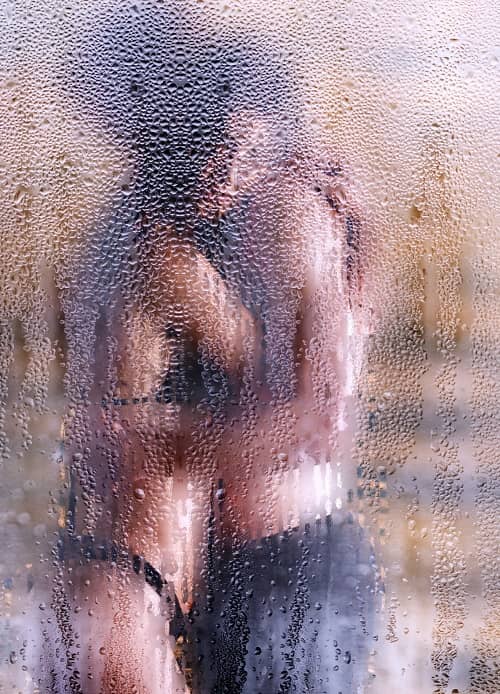 Ein Päärchen steht hinter einer nassen Duschwand und kuscheln